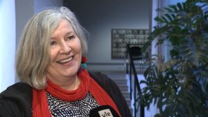 Riitta Kormano. Riitta Kormano, en dam med gråsilvrigt hår och röd halsduk, ler stort.