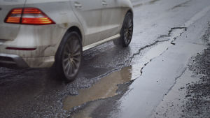 Beläggningsskadorna förvärras under snöfattiga vintrar. en bil kör förbi en lång och djup beläggningsskada