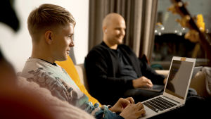 Ilari on ammatiltaan erityisopettaja ja uravalmentaja, Jukka puolestaan työyhteisövalmentaja, luennoitsija ja videotuottaja. kaksi iloista miestä työskentelevät työpaikan sohvalla läppärien kanssa