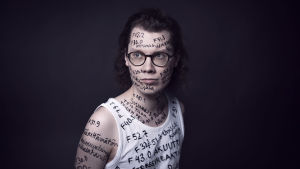 PItkähiuksisen radiotoimittaja Jani Tanskasen kasvoille ja iholle sekä hihattomaan paitaan on kirjattu psykiatristen diagnoosien nimiä ja koodeja tautiluokituksesta ICD-10.