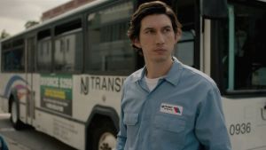 Adam Driver ajaa bussia ja runoilee elokuvassa Paterson. Bussinkuljettaja Paterson (Adam Driver) hieman huolestuneen näköisenä bussinsa ulkopuolella elokuvassa Paterson