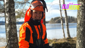 Arja Koriseva hymyilee kameralle metsämaisemassa metsurivarusteissa ja raivaussaha käsissään.