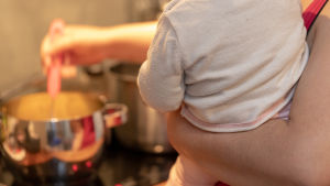 Om barnet har svårt att äta för att näsan är för täppt kan det vara skäl att söka vård, råder läkare. En mamma rör om i en kastrull med ett barn i famnen.