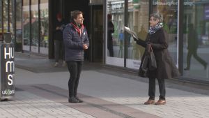 Konsta håller avstånd till sina kunder. En gatuförsäljare pratar med en dam på en kall gågata.