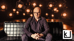 Toimittaja J.P. Pulkkinen istuu sohvalla ja katsoo tiukasti kameraan. Kuva on otettu Tleveision tiiliskivet -sarjaa varten. 