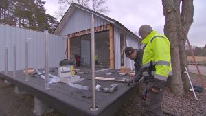 Nytt byggs i gästhamnen Verkan i Korpo. Två män i byggoveraller står framåtböjda vid ett husbygge.