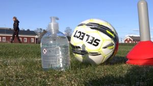 En handdesinficeringsflaska och en fotboll står på en gräsplan.