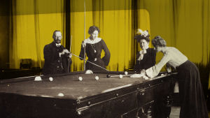 Kuvassa kolme naista ja yksi mies pelaavat biljardia 1800-luvulla.