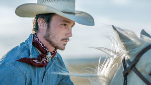 Nuori cowboy ratsastaa valkealla hevosella stetson päässään.