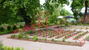 En dekorativ skulptur och miljökonstverk till minne av Pehr Kalm. Röd skulptur av metall kring en trädgård.