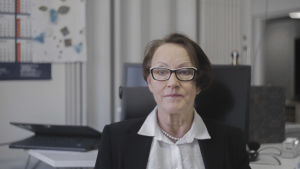 Hannele Rämö är verksamhetsledare för Asumisterveysliitto. En kvinna sitter i ett kontor. Hon ser in i kameran och ser bestämd ut.