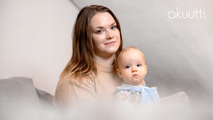 Jenni Tamminen istuu pieni tytär sylissään vaaleassa huoneessa. Molemmat katsovat kameraan.