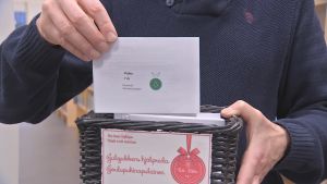 En 7-årig pojke önskar sig små plastsoldater. En person med blå tröja drar upp ett kort ur en liten låda med julklappsönskemål. På lappen står att en 7-årig pojke önskar sig små plastsoldater.