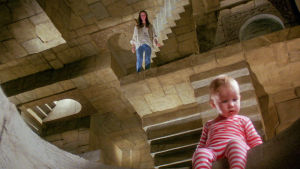 Sarah ja pikkuveli labyrintissä. Vauva istuu mielikuvituksellisessa labyrintissä, taustalla nuori tyttö. Kuva elokuvasta Labyrintti.