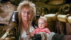 David Bowie antoi luvan vaihtaa rooleja. Peikkokuningas Jareth vauva sylissään. Kuva elokuvasta Labyrintti.