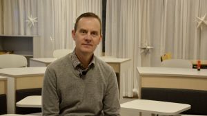 Rektor Mikael Fröjdö välkomnar den utvidgade läroplikten. Mikael Fröjdö sitter på en stol i en modern lärmiljö med bord som är ordnade som en hästsko i rummet.
