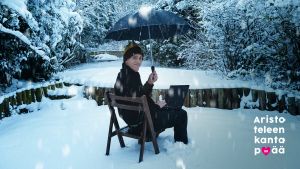 Hymyilevä mies istuu tuolilla lumihangessa läppäri sylissään ja sateenvarjo kädessään.