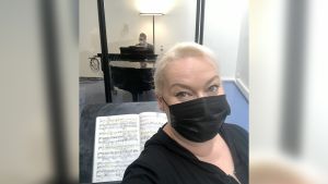 Oopperalaulaja Johanna Rusanen-Kartano mustassa maskissa, taustalla Kansallisoopperan harjoituspianisti Hans-Otto Ehrström.