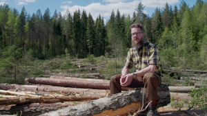 Metsäkoneyrittäjä Tero Kurula istuu hakkuuaukiolla kaadettujen tukkien päällä kesäisenä päivänä. 