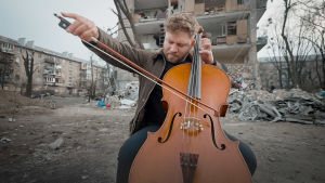 Lukas Stasevskij soittaa selloa tuhoutuneen kerrostalon edessä.