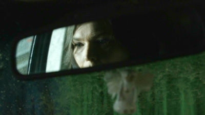 Kvinnas ansikte i backspegeln på en bil.