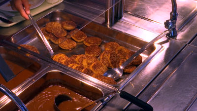 Någon tar maletköttbiffar i en skolmatsal.