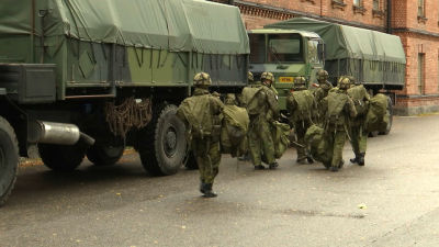 militär med packning invid lastbilar