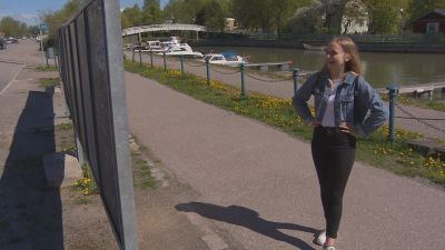 Desirée Kavander, en ung dam med jeansjacka och ljust hår, står med armarna i sidorna och tittar på en ställning för valaffischer.