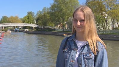 Desirée Kavander, en ung dam med jeansjacka och ljust hår, står vid en hamn med båtar.