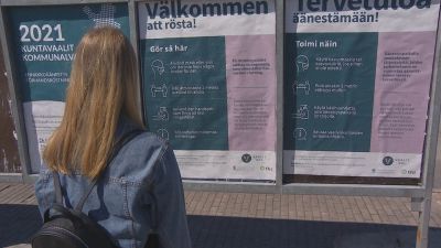 En ung dam med långt ljust hår och en jeansjacka ser på uteaffischer om hur kommunalvalet 2021 går till.