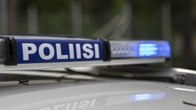 Närbild på polisskylt med blåljusen på i en polisbil.