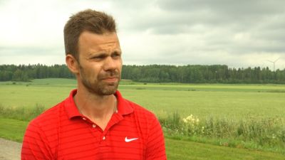 En man med röd pikétröja står vid en grönskande åker.