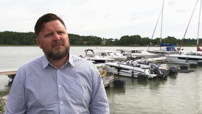 En man i blårandig skjorta står framför en brygga med båtar.