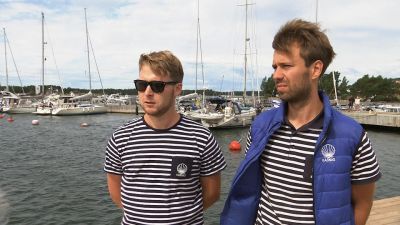 Två unga män står framför en brygga med båtar.