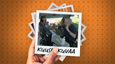 Yläviistosta kuvattuna toimittaja Vesa Kytöoja ja pianisti Ralf Gothóni kesäisellä pihamaalla keskustelemassa iloisesti. Miesten edessä pöydällä on tv-monitori ja toimittajan korvilla kuulokkeet.