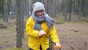 Minna Söderholm tycker att städningen skapar gemenskap i gruppen. Minna Söderholm i gul regnjacka i en skog med en kratta i händerna.