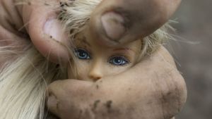 Våldet och oron i karaktären Brunos vardag sätter nästan inga spår i karaktären, enligt recensenten Adrian Perera. Smutsig hand klämmer Barbie-docka.