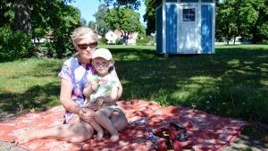 Birgitta Bruce sitter på en filt på stranden med sitt barnbarn, Ellen Karlsson. Birgitta Bruce och Ellen Karlsson