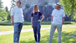 (Fr.v.) Per Fallenius, Elina Lehtikangas och Riggert Munsterhjelm lovordar Snappertuna. Tre personer, två män och en kvinna, framför en medeltid slottsborg en sommardag.
