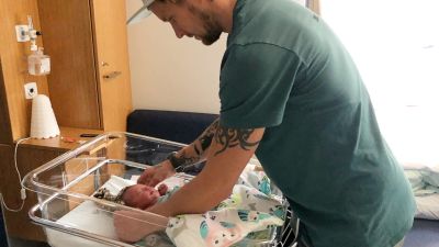 Antti Annala sätter på mössan på sin nyfödda dotter som ligger i sjukhusets säng.