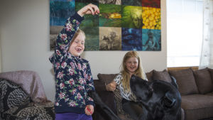 Två av familjen Saarinens fem barn, Adessa och Eeden leker med en av familjens hundar Milou. Två flickor leker med en svart hund.