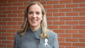 Sandra Bergqvist hoppas att det här kan leda till att den svenskspråkiga vården i Egentliga Finland utvecklas. En leende Sandra Bergqvist iklädd grå rock ståendes framför en röd tegelvägg.