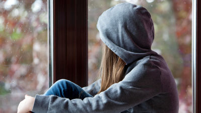 En ung kvinna sitter vid ett fönster och tittar ut.