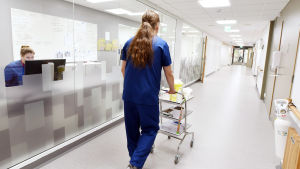 Finländarna har enligt studier väldigt höga tankar om yrken inom vårdsektorn. Manlig sjukskötare går i korridor på Mellersta Österbottens Centralsjukhus i Karleby. En kvinnlig anställda sitter bakom en datorskärm i ett intilliggande rum med stora fönster som vetter mot korridoren.