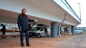 Jan Gröndahl visar var vindskyddet kommer att byggas och taxibilarna kommer att kunna stanna. Man med mörkt hår står vid en bro och pekar åt vänster.