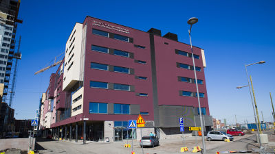 På bilden ser man ett stort vinrött hus. Huset är en hälsocentral.