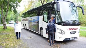 Närmare 30 passagerare stiger ombord under bussturen runt Kimitoön. En buss står parkerad på en sandplan i vackert, men mulet höstväder.