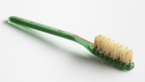 Tidig industriell produkt med skaft av plast. Gammal tandborste med skaft av grönt plast.
