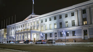Helsingfors stadshus. Helsingfors stadshus. Det är en mörk vinterkväll. På gatan utanför stadshuset står bilar på rad. På gatan ligger snö.