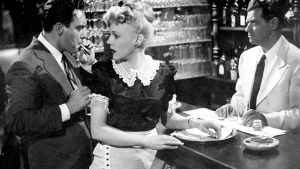Kino Klassikko: Kaksoiselämää. Mies ja nainen ovat baaritisklillä, nainen tarjoilijan asussa. Baaritiskin takana on mies valkoisessa puvussa.